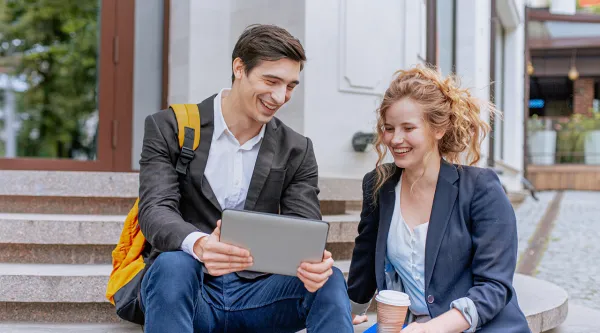 A male and female sitting outside on steps looking at a tablet and smiling
