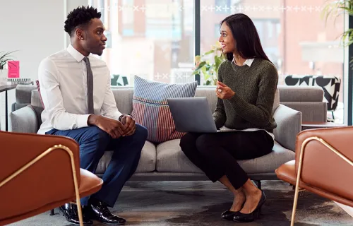 two people sit on sofa having discussion with a laptop