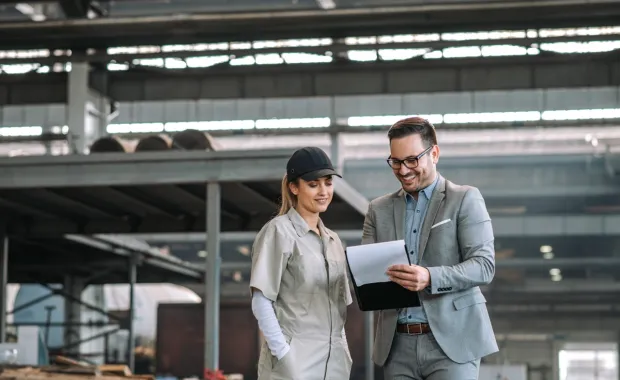 Manager and employee talking at manufacturing factory while looking at a tablet